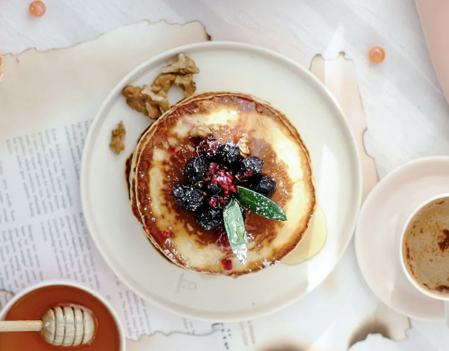 A stack of pancakes with berries and nuts on a white plate

Description automatically generated