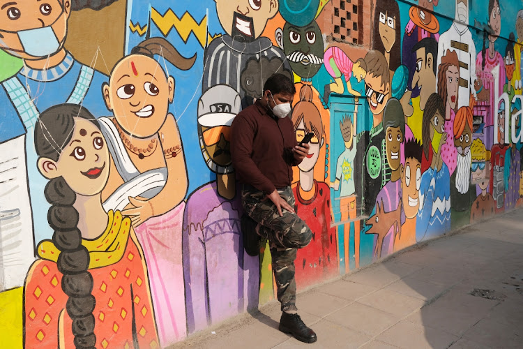 A man wearing a protective mask looks at a smartphone while leaning against a mural at Khan Market in New Delhi, India. File phto: BLOOMBERG/T. NARAYAN