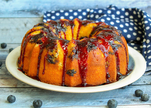 Blueberry bundt cake on a plate with blueberries sprinkled around.