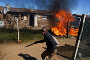 A man holding a machete reacts next to a fire after community members burned shacks and belongings as they searched for alleged illegal miners known as ‘zama-zamas’ as a protest, following alleged rape of eight models on July 28 when a television crew filmed a music video at a mine dump in the nearby township, in the West Rand, South Africa, August 8, 2022.