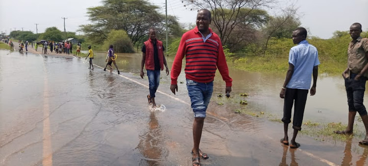 Tiaty MP William Kamket (in maroon sweeter) rolls his pair of jean trousers to wade through flooded road section in Loruk, Baringo North after Lake Baringo burst on Tuesday.