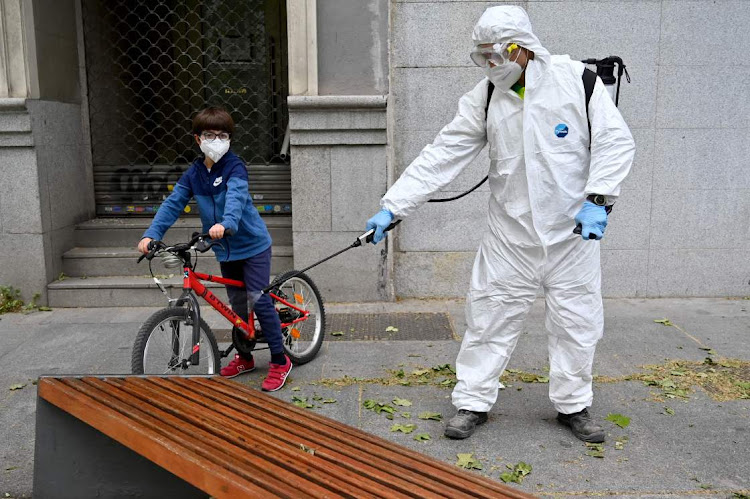 A boy wearing a face mask rides his bike next to a worker disinfecting a bench in Madrid on April 28, 2020 during a national lockdown to prevent the spread of the Covid-19 disease. Spain recorded a slight decrease in the number of daily coronavirus deaths with the government set to unveil plans to relax stringent lockdown measures in place since mid-March.