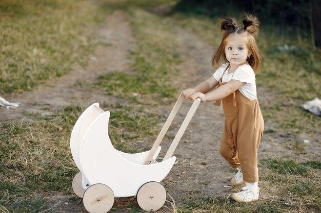 Free photo cute little girl playing in a park with white carriage