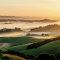 Item logo image for A sunrise over a valley with fog and hills