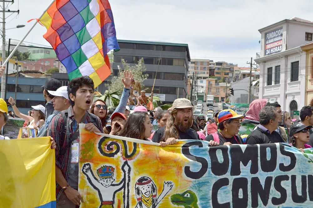 Ecuadorians hold banners and chant in a public square