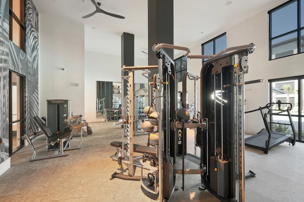 Community resident fitness center with treadmills, weights, high ceilings, and large windows for natural sunlight