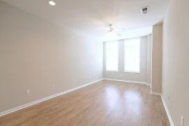 Living room with tall ceilings, wood flooring, two large windows, and a neutral color scheme