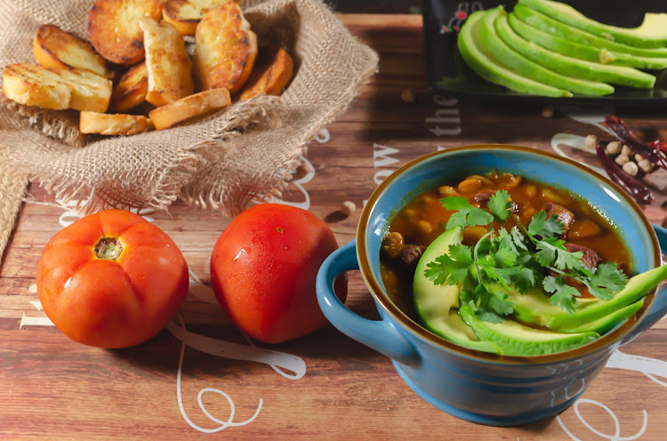 Stew of chorizo and chickpeas with avocado and toast garnished with cilantro.