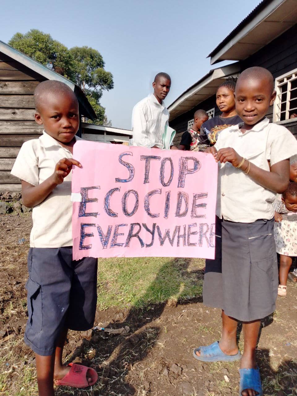 Two young children in school uniform hold a sign that says 'stop ecocide everywhere'