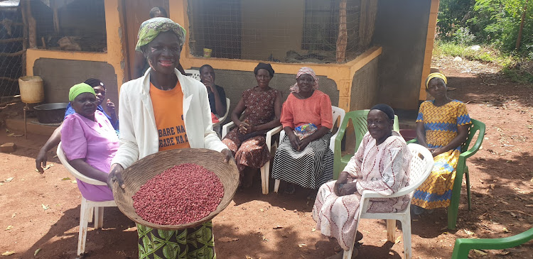 Doreen Auma, a farmer, who doubles up as Mapor Mayier Farmers Group secretary shows a sample of groundnuts they produce as the other members look on.