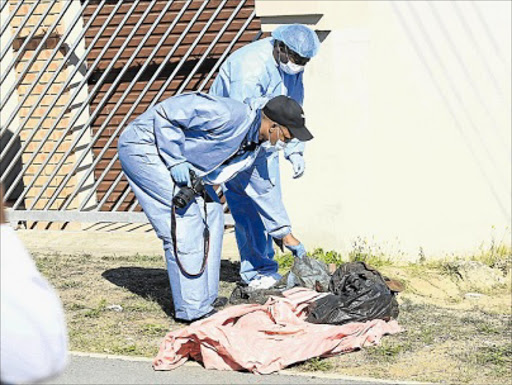 WRAPPED IN CURTAIN: Members of the Department of Health’s forensic unit examine the decomposed body that was found in front of a Mdantsane house yesterday morning Picture: SINO MAJANGAZA