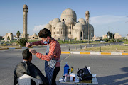 A barber, wearing a face mask to curb the spread of Covid-19, cuts the hair of a policeman near the old bridge in the old city of Mosul, Iraq, on April 18 2020. 