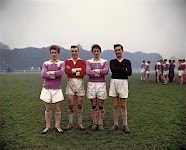 4 staande mannen in vuil sporttenue op een grasveld