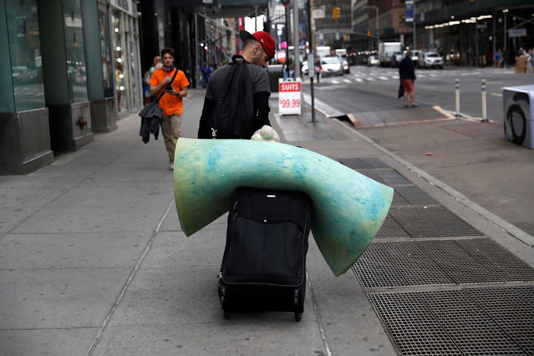 A man walks with a suitcase and a cushion mattress near Times Square in New York City, US, June 11, 2021.