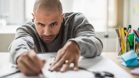 a man working with ruler and pen on a table with a large sheet of white paper and some cups of colorful pens