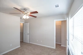 Bedroom with a ceiling fan, walk-in closet, window on the right, neutral walls, and neutral carpet