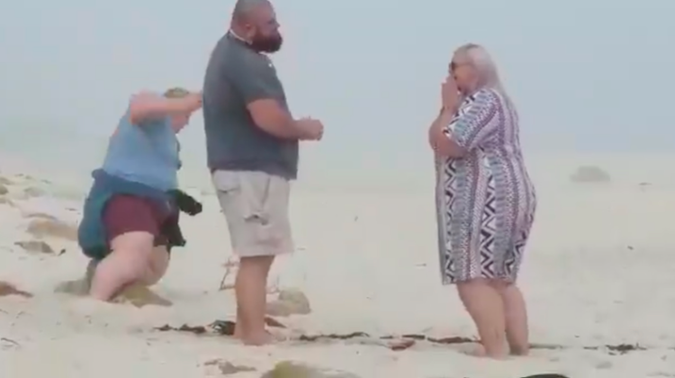 The photographer falls while trying to capture a proposal at the beach.