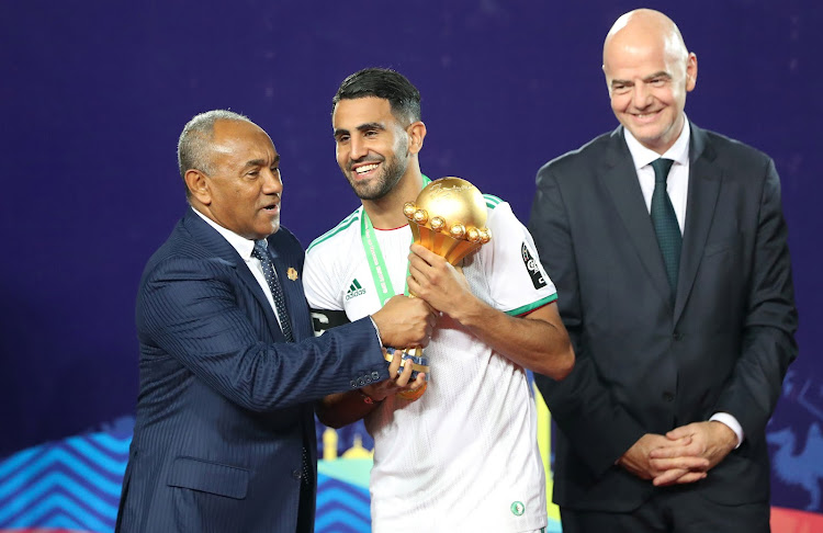 Algeria's Riyad Mahrez (C) receives the trophy from Caf President Ahmad Ahmad (L) after winning the Africa Cup of Nations in July 2019 as Fifa President Gianni Infantino looks on.