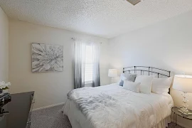 Model bedroom with gray carpet, window with blinds, and bedroom furniture