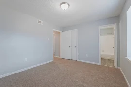 Empty apartment room with beige carpet, light gray walls, and white doors.