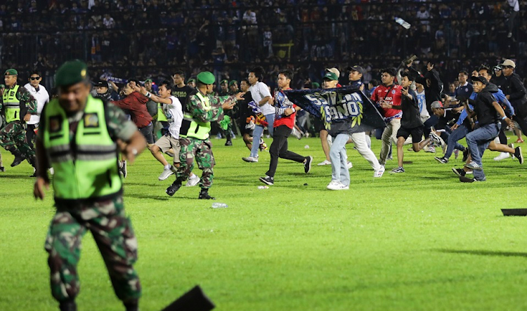 Soccer fans enter the pitch as military personnel try to stop them during a riot following a soccer match at Kanjuruhan Stadium in Malang, East Java, Indonesia on October 1 2022. At least 174 people including police officers were killed after fans entered the pitch causing panic and a stampede.