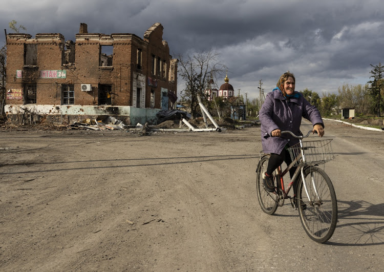 A woman rides her bicycle past destroyed buildings on October 5, 2022 in Drobysheve, Ukraine.