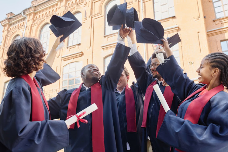 A group of students in robes raising their hats up and celebrating their graduation.