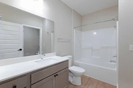 Bathroom with neutral vanity with lower cupboards and drawer next to the toilet and shower/tub combo with a curtain rod.