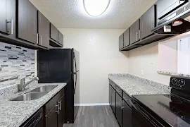 Modern kitchen in an apartment with granite countertops, black appliances, and dark wood cabinets.