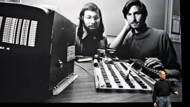 Steve Jobs in front of screen showing him with Steve Wozniak in the early days.