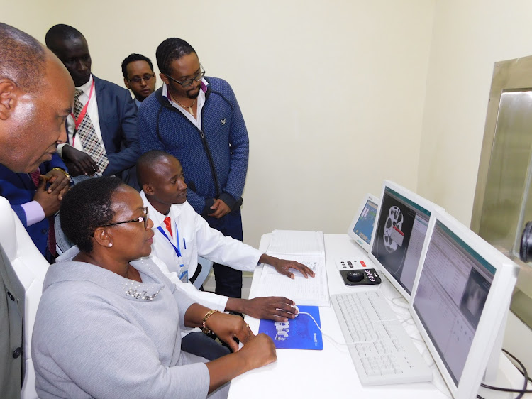 Governor Francis Kimemia watches as JM Memorial Hospital radiographer Fredrick Mwirigi shows Health CS Sicily Kariuki how the CT-Scan equipment works.