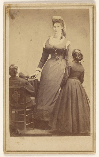 [Anna Swan standing in front of two average sized people.] (Main View)