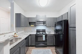 Kitchen with dark gray cabinets, black appliances, stainless microwave, stone countertops, and wood plank flooring