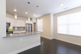 Living room facing kitchen with multiple windows, wood inspired floors, and neutral walls