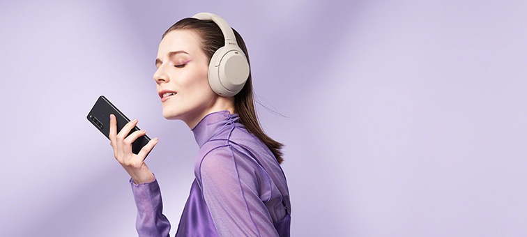 A woman wearing headphones and holding an Xperia 10 IV