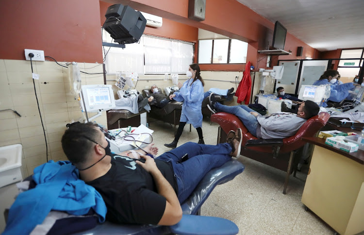 A healthcare worker walks past men recovered from the coronavirus disease (COVID-19) donating convalescent plasma, at the Hemotherapy Institute in La Plata, Argentina October 5, 2020.