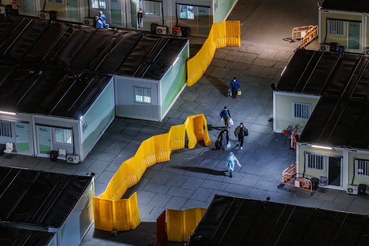 A healthcare workers wearing personal protective equipment (PPE) escorts patients through a Covid-19 isolation facility in the Tsing Yi area in Hong Kong, China, on Tuesday, March 8, 2022.