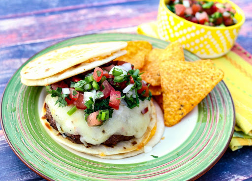 Quesadilla burger with pico de gallo and chips on a plate.