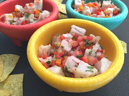 Three bowls filled with ceviche sitting on a black table mat with tortilla chips around.