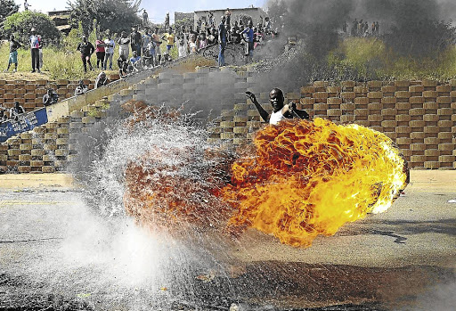 A protester swirls around a burning tyre during one of service delivery protests. The writer says political parties will need to convince voters next year on how they will turn things around.