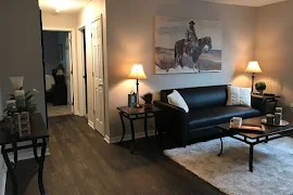 Furnished living room with wood-inspired flooring, beige walls, next to hallway leading to bedroom