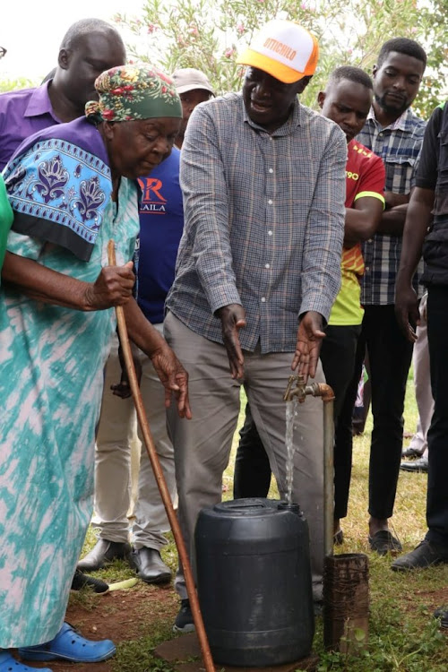 Governor Wilber Ottichilo helps an elderly woman draw water in Mazuu