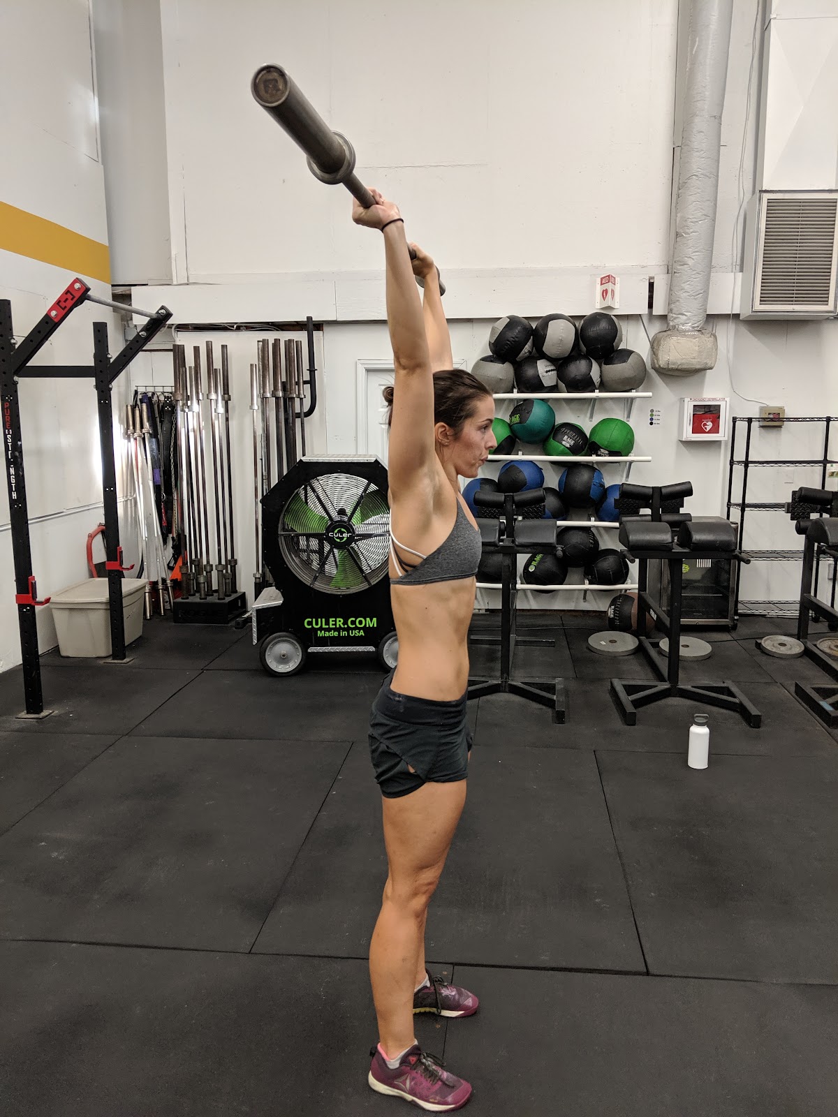 woman in gym with barbell pressed overhead