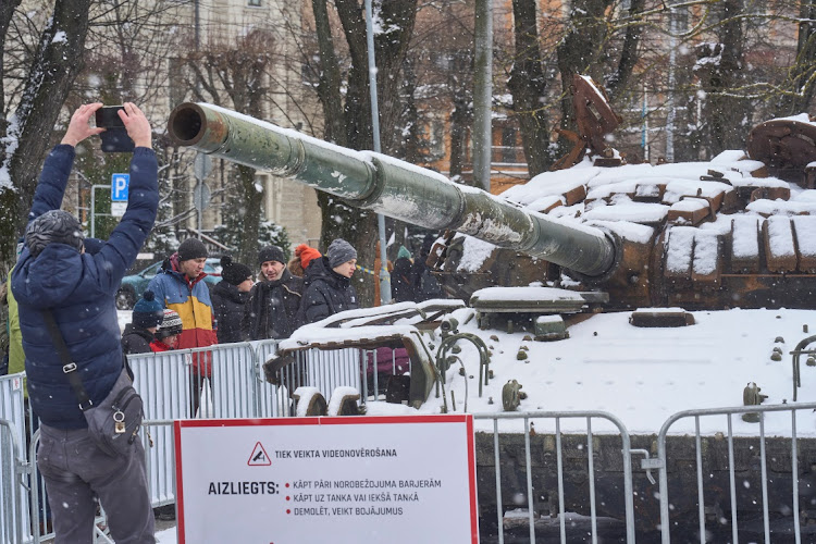 A man takes a picture of the destroyed Russian T-72B tank, secured from the Ukrainian village of Dmytrivka, outside Kyiv, on display in front of the Russian embassy in Riga, Latvia.