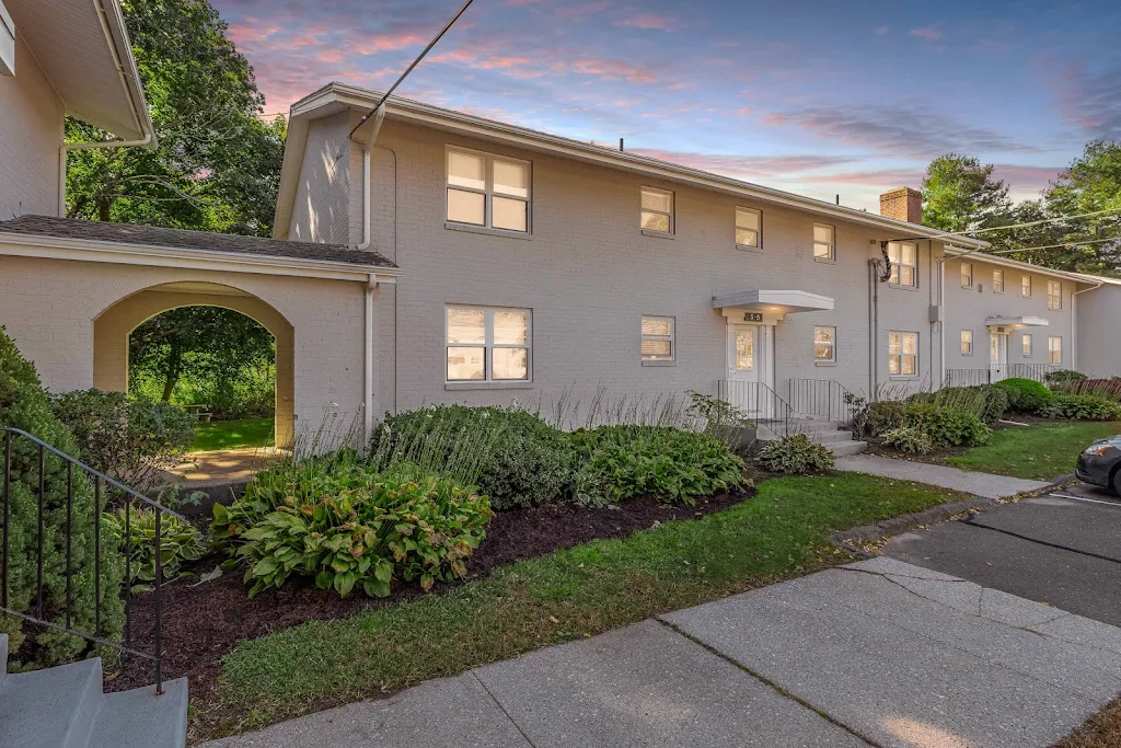 Apartment complex with neutral exterior and landscaping with shade trees behind at dusk.