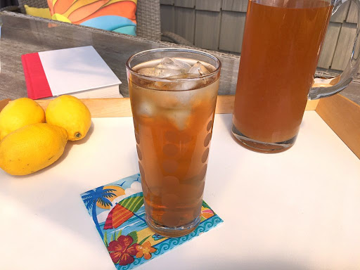 A tall glass filled sitting on a tray with iced tea along with lemons.