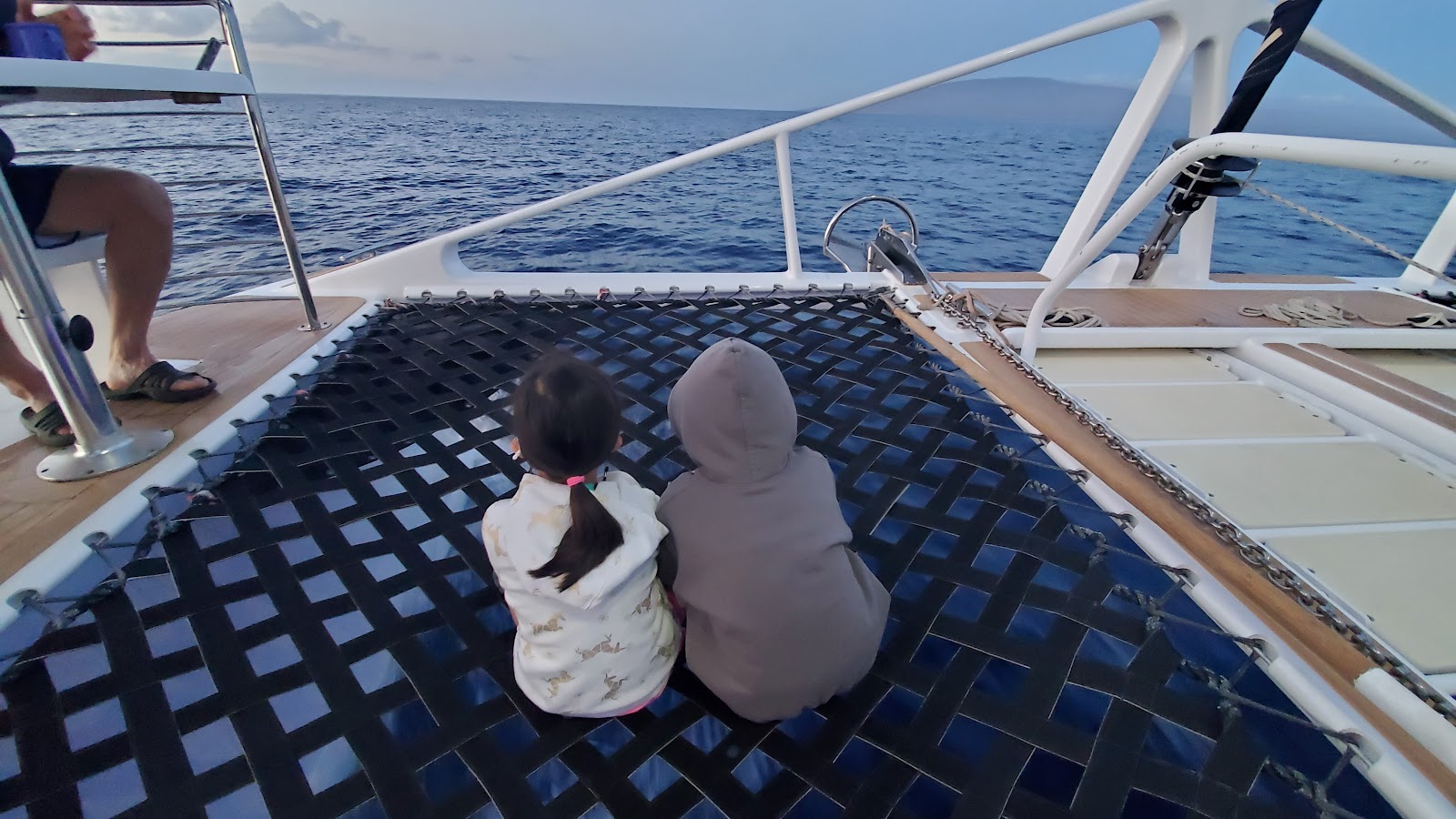 Image of two girls sitting on black netting on a boat traveling from Maui to Lanai.