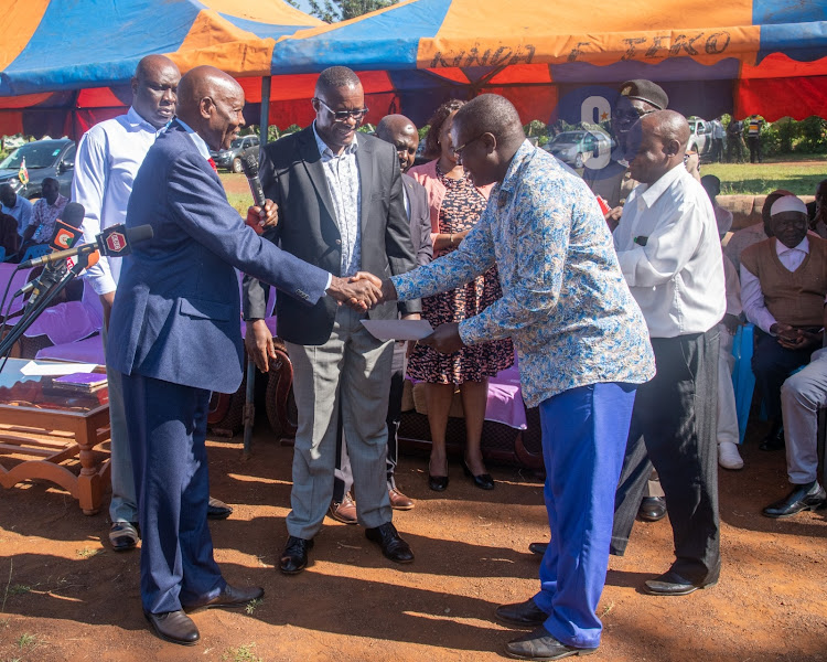 Education CS Ezekiel Machogu and his ICT counterpart Eliud Owalo handing over a form showing their commitment to deliver Sh2 million towards the school's development to the management of Kametho Primary School in Rarieda on May 30, 2023