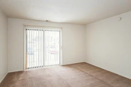 Living room with white walls and trim, neutral carpet, sliding glass door with blinds