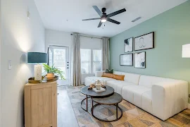 Modern apartment living room with white sofa, circular coffee tables, mint walls, and balcony door.